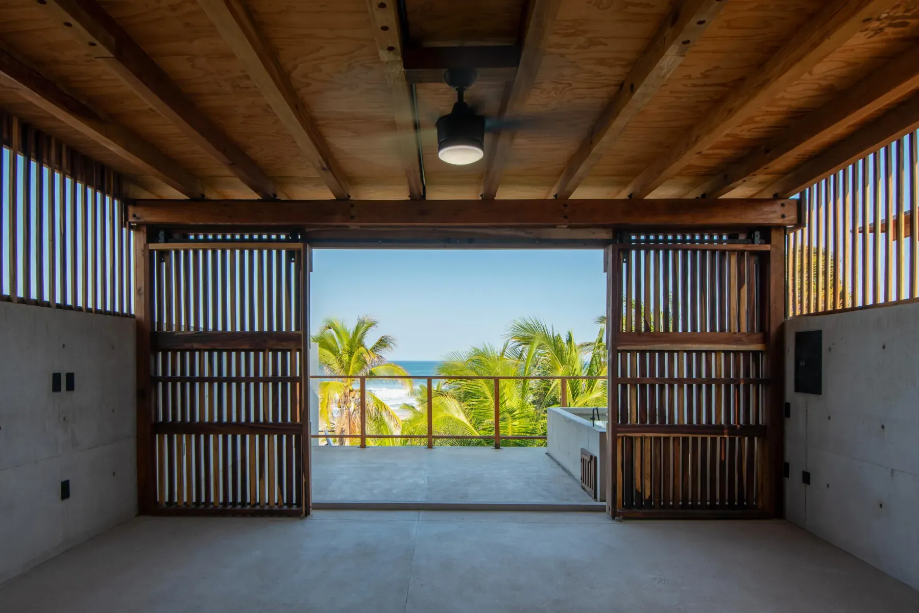 Interior de Paxifico con celosías de madera y vista al mar entre palmeras